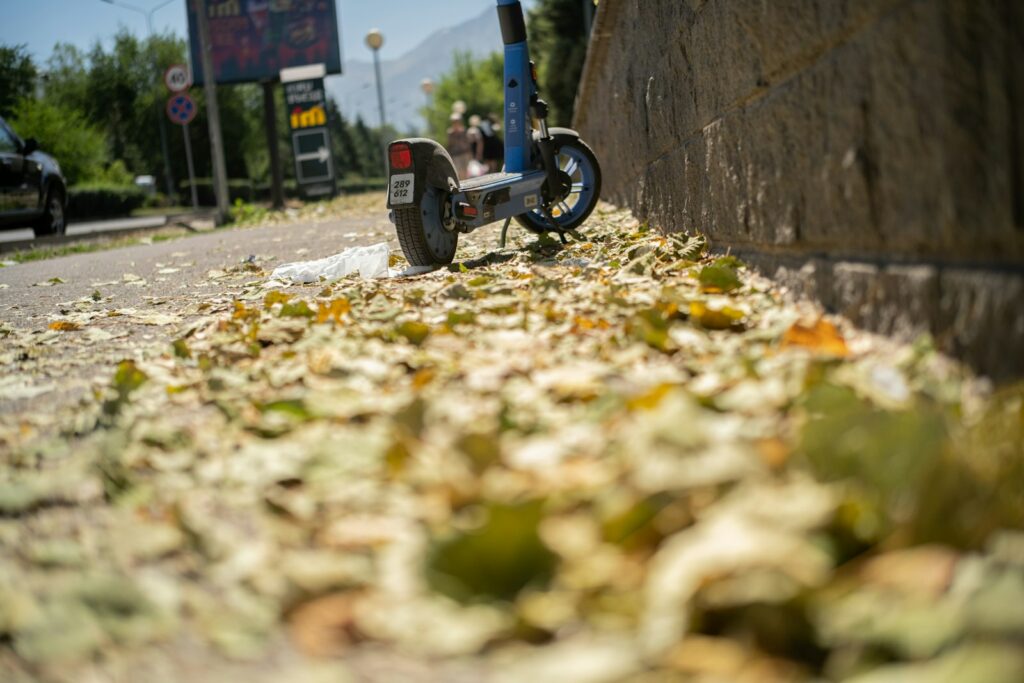 Trottinette électrique en hiver, garée sur un trottoir couvert de feuilles mortes